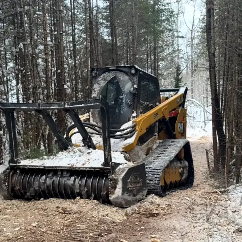 Tracked loader with a forestry mulching head cutting a trail through snowy pines