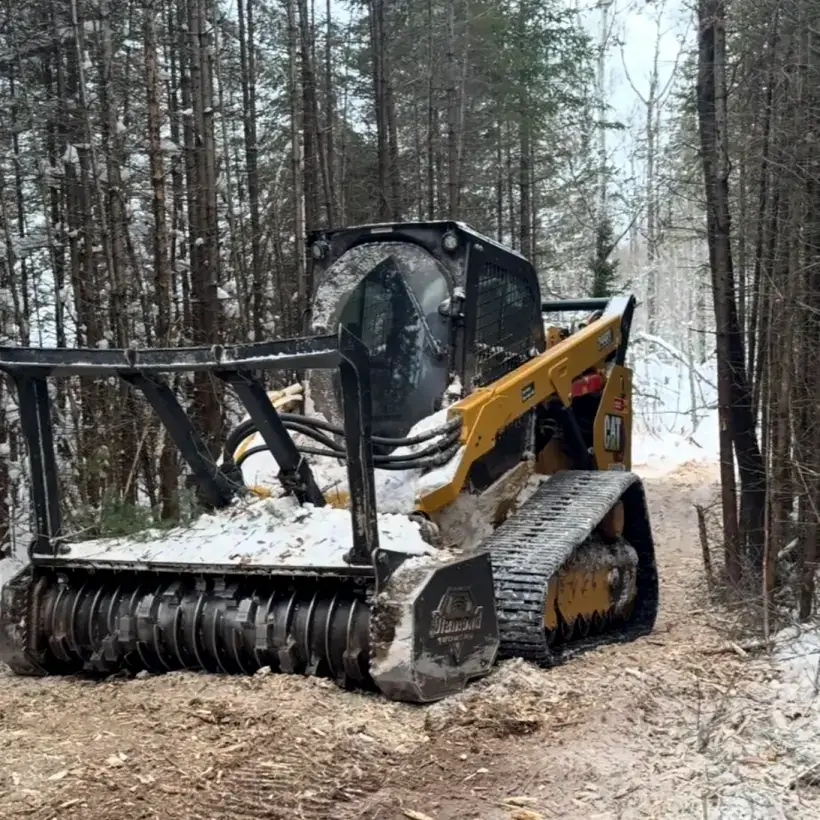 Tracked loader with a forestry mulching head cutting a trail through snowy pines
